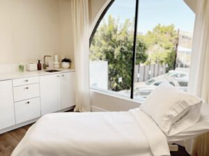 Simple and elegant patient room with a bed, cabinets, and a window looking out upon a serene view